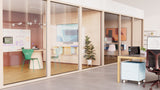 A photo taken from an open plan office space, facing two meeting rooms. In both meeting rooms, underneath the TVs, are visible Logitech Rally Bar Huddle cameras.