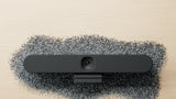 A front-facing image of the Logitech Rally Bar Huddle lying in what appears to be plastic pellets, a reminder that this camera is produced using post-consumer recycled plastics.