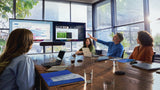 A picture of a meeting room. Four people are sitting at a table, looking towards two TVs placed at the front of a meeting room. The left TV shows somebody’s calendar and the right shows the content being presented as well as other meeting participants on the call. There are two black HP Poly Studio A2 microphones along the centre of the table.